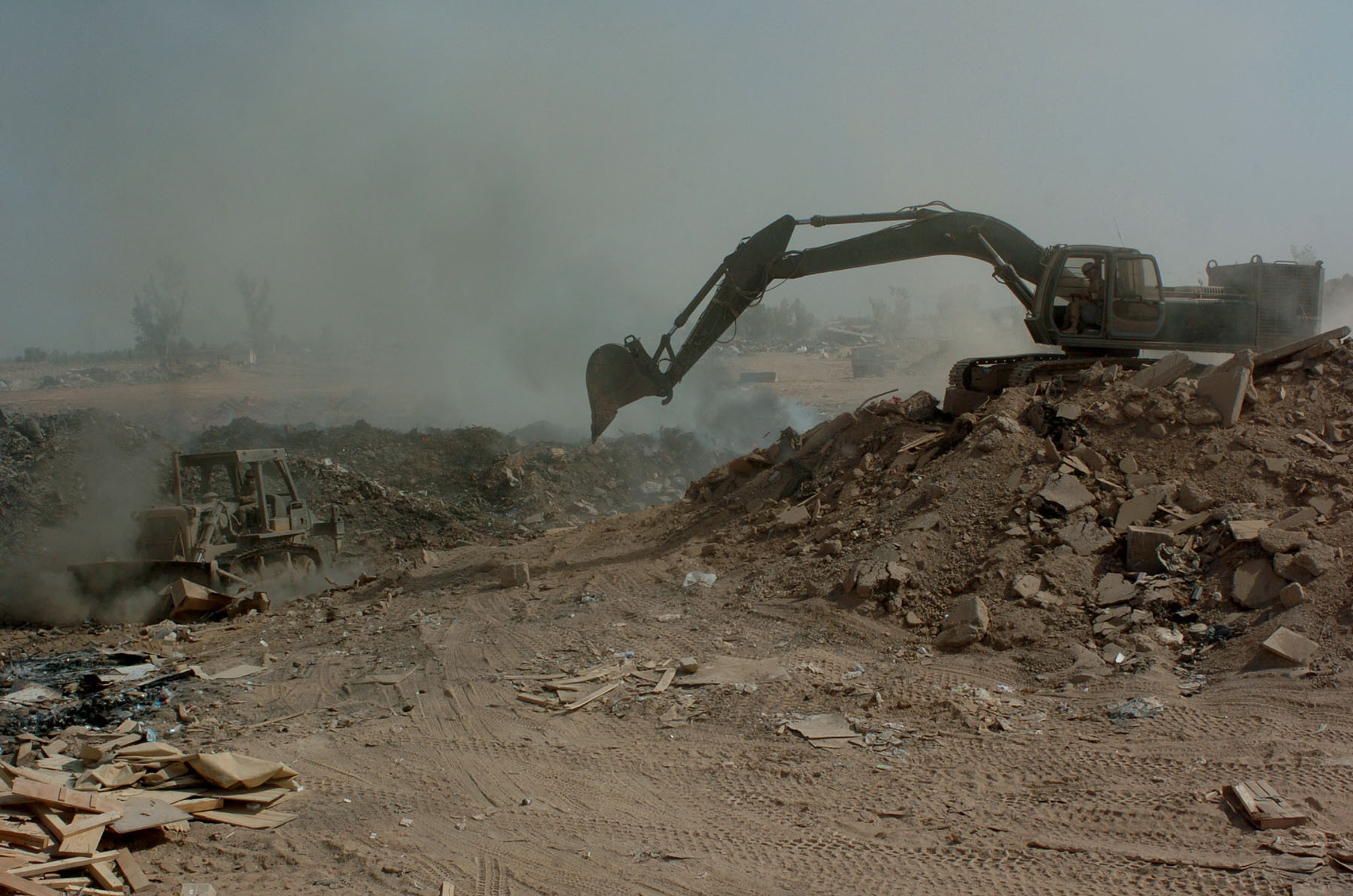 Soldiers from the 84th Combat Engineer Battalion use a bulldozer and excavator to manuever trash and other burnable items around in the burn pit at the landfill here. The bulldozer is primarily used to keep refuse constantly burning, and the excavator to push dirt over chutes to make the land useable in the future. (Courtesy Photo)