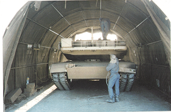 Figure 5. A member of the 325th Maintenance Company spray paints desert tan CARC onto a tank