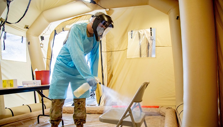 Image of Man in full PPE spraying down a chair with sanitizer.