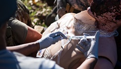 Military personnel participating in training exercise, treat a dummy for injuries