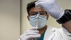 Medical personnel filling a syringe from a vaccine bottle