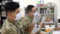 Two healthcare workers, wearing masks, adding the COVID-19 vaccine to syringes