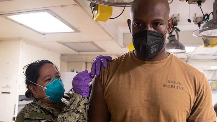 Image of Hospital Corpsman 1st Class Mary Ashcraft, assigned to the combat ship USS Tulsa, administers a COVID-19 vaccine booster to Aviation Machinist Mate 1st Class Anthony Johnson Jan. 10, 2022, at Apra Harbor, Guam. (Photo: Mass Communication Specialist Petty Officer 1st Class Devin M. Langer, Command Destroyer Squadron 7).