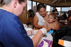 Medical technician pricks the finger of child while his mother holds him