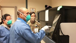 Three lab technicians in full PPE looking at computer screen