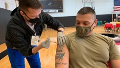 Marine on right gets a COVID-19 booster vaccination from a nursing student on his left.