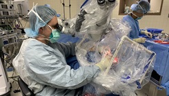 Two medical personnel, wearing full PPE, in an operating room