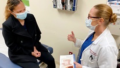 A patient sits in an office with while a health care provider talks to her.