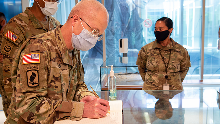 Military Personnel wearing a face mask signing a book 