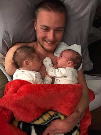 Image of Jason Hallett holding his infant twin babies. 