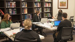 A group of military health personnel wearing face masks sitting around a table using laptops