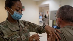 Military health personnel wearing a face mask administering the COVID-19 vaccine