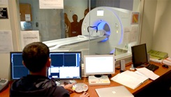  U.S Navy MRI technologist behind a computer screen with a magnetic resonance machine in the background.