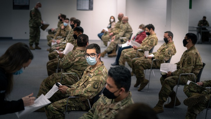 Image of Military personnel wearing face mask sitting in a line waiting for their COVID-19 vaccine.
