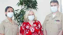 Two military personnel, wearing masks, standing with woman in red dress, also wearing a  mask