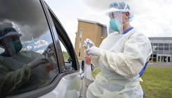 Military personnel in full PPE at a car window demonstrating a swabbing technique