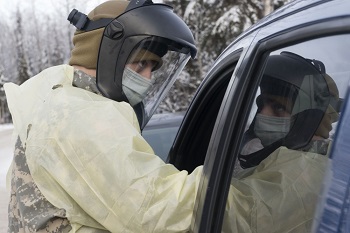 Healthcare worker, wearing personal protective gear, leans into a car at a pharmacy drive-thru