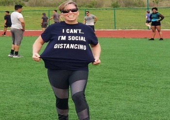Woman on baseball field wearing a t-shirt that says "I can't -- I'm social distancing."