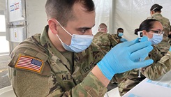 Military personnel wearing a face mask filling up syringes with the COVID-19 vaccine