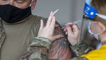 Military personnel wearing a face mask administering the COVID-19 vaccine