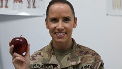 A female soldier poses with an apple in her hand.