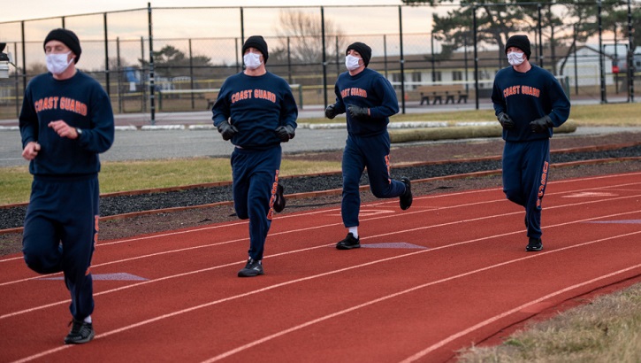 Four military personnel, wearing masks, running on a track