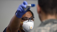 Medical personnel scanning forehead of soldier with thermometer